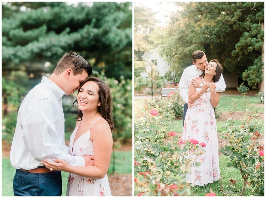 A man kisses his fiancee on the cheek in a rose garden filled with golden glowy light.