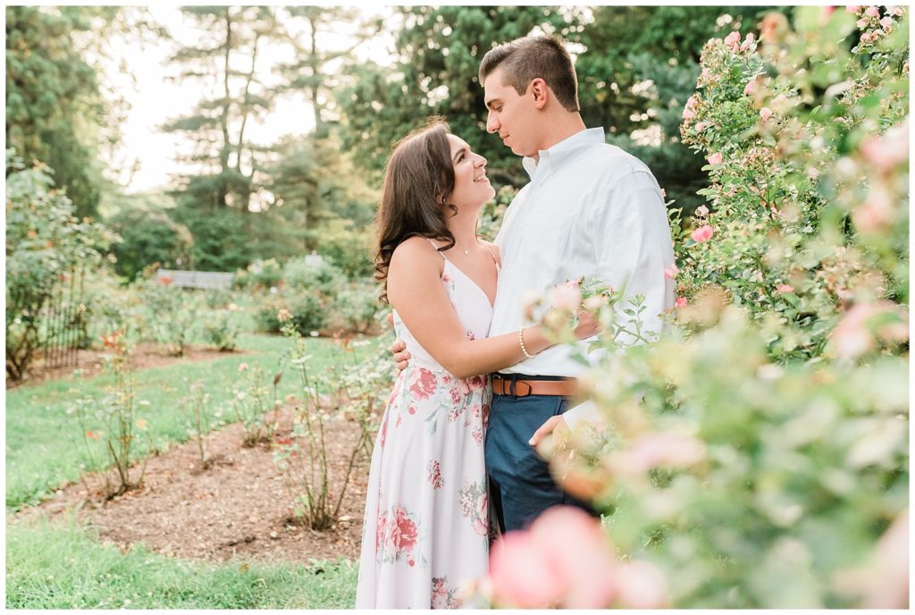 A couple hugs in a rose garden among blooming flowers.