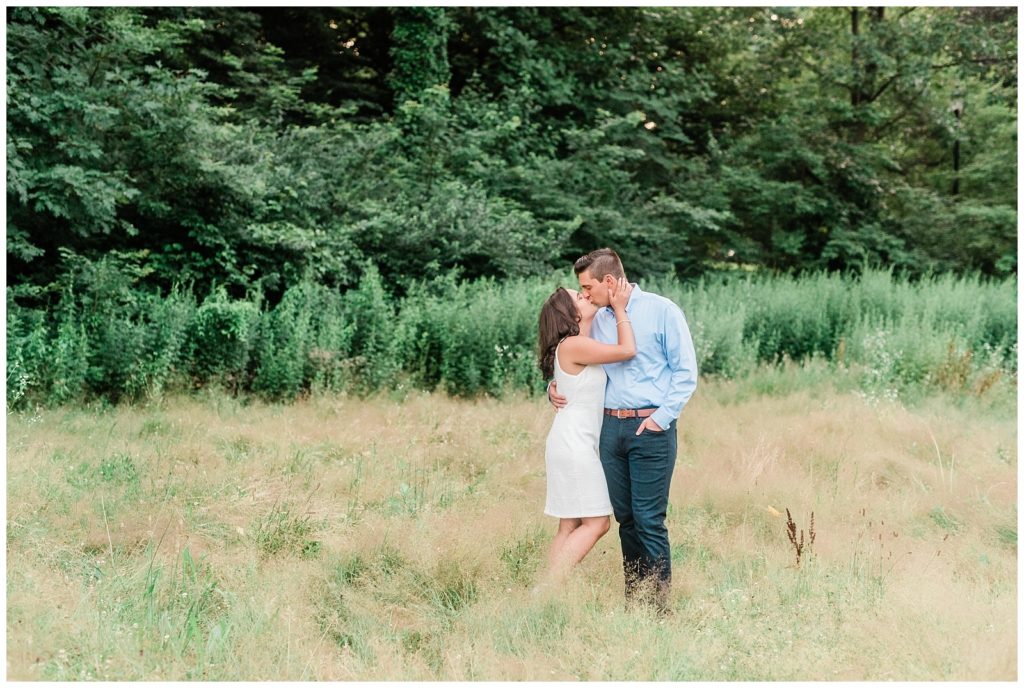 A couple kisses in a field of tall grass.