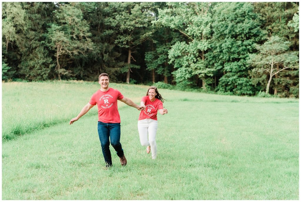 A couple wearing Rutgers T shirts runs through a field.