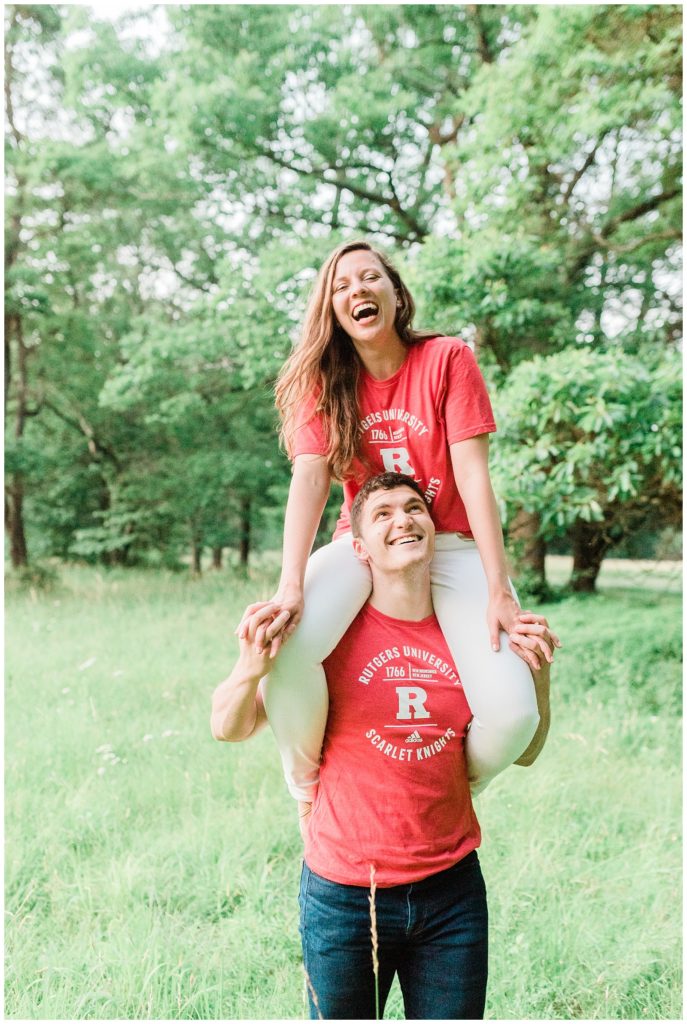 A woman wearing a red Rutgers shirt sits on the shoulders of a man wearing a red Rutgers shirt.