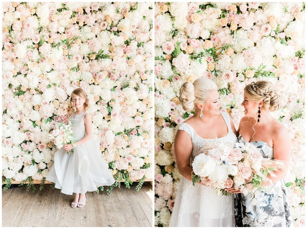 The flower girl stands in front of a flower wall.