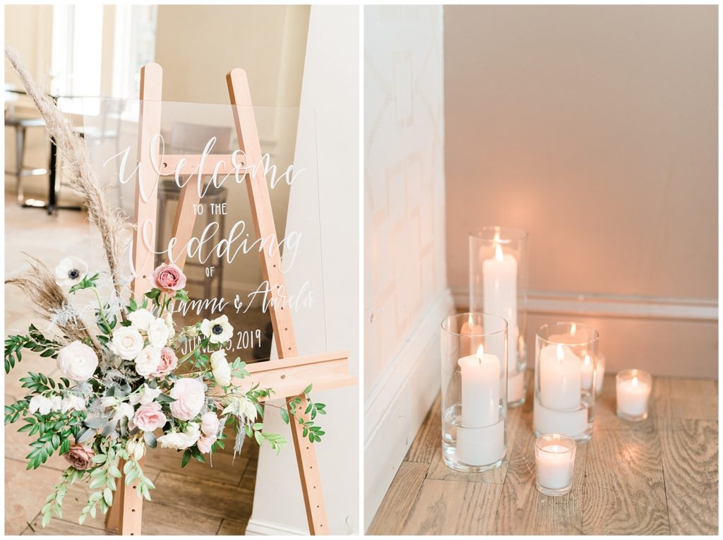 A clear acrylic welcome sign with white calligraphy sits on an easel with florals in the corner.