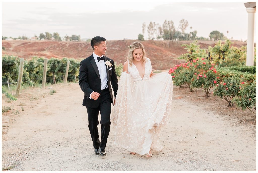 A bride and groom hold hands walking through the vineyard at Avensole Winery in Temecula, California.