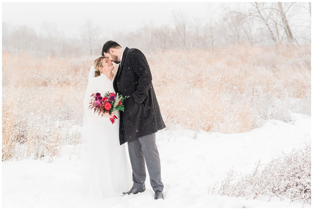 A bride and groom rest foreheads together as the snow falls around them in Beacon NY at Roundhouse Hotel winter wedding inspiration.