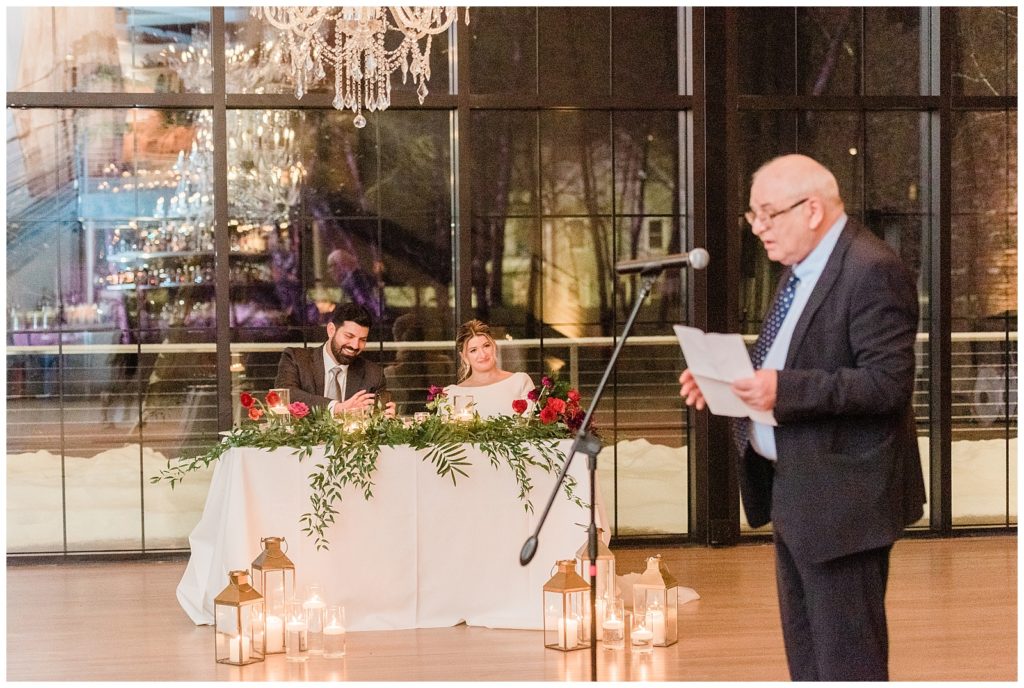 Father of the bride gives a speech while bride and groom listen from their sweetheart table at their winter wedding in Beacon NY at Roundhouse Hotel winter wedding inspiration.in Beacon NY at Roundhouse Hotel.