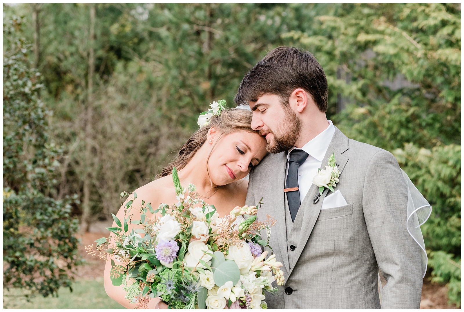 Bride resting her head on the groom's shoulder while holding a wild flower bouquet.