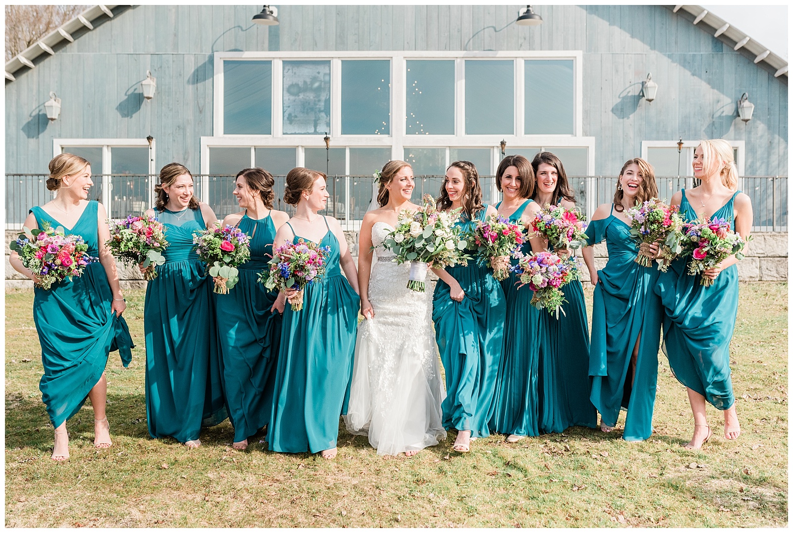 Bridesmaids wearing teal dresses holding colorful bouquets, walking and laughing next to the bride.
