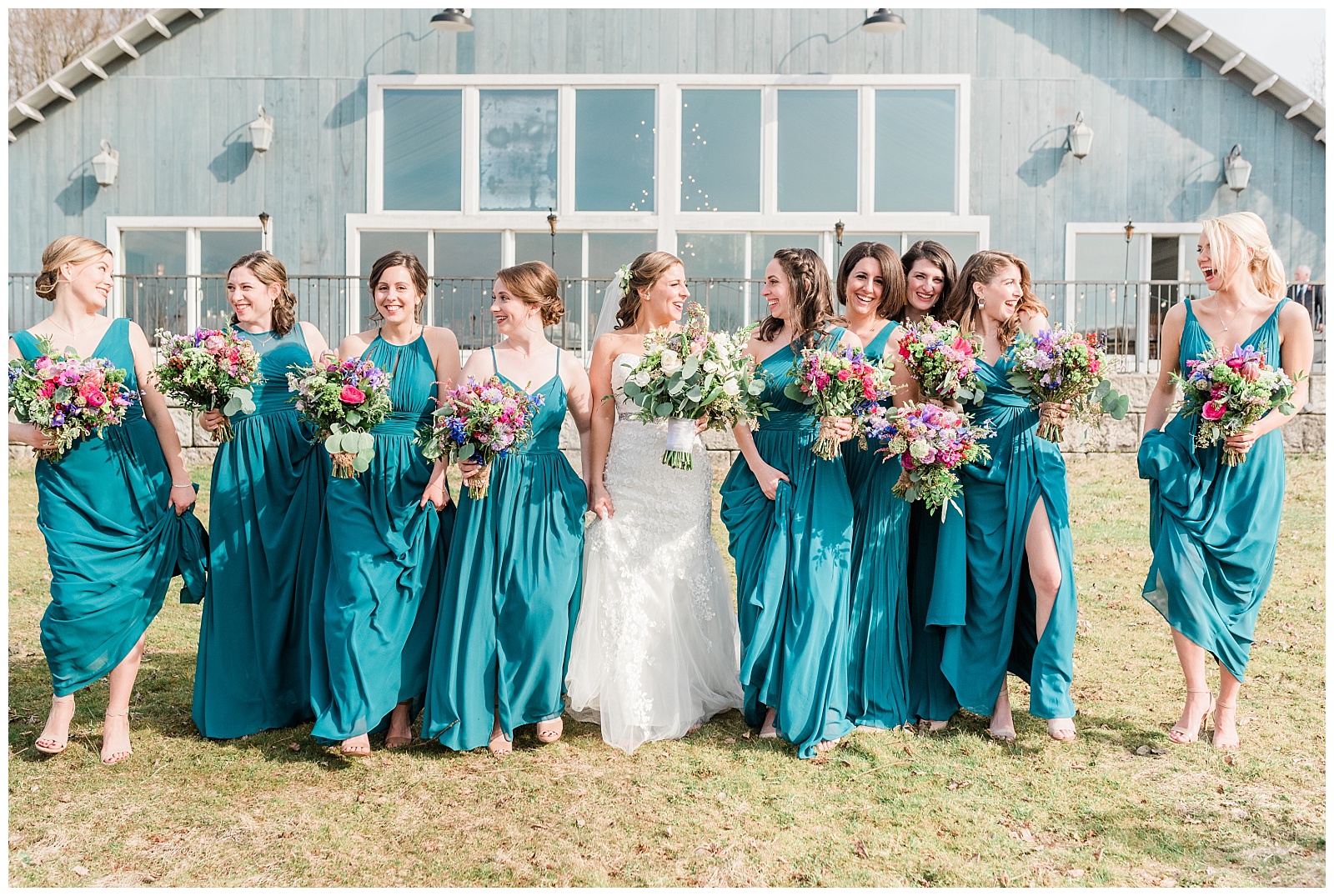 Bridesmaids wearing teal dresses holding colorful bouquets, walking and laughing next to the bride.