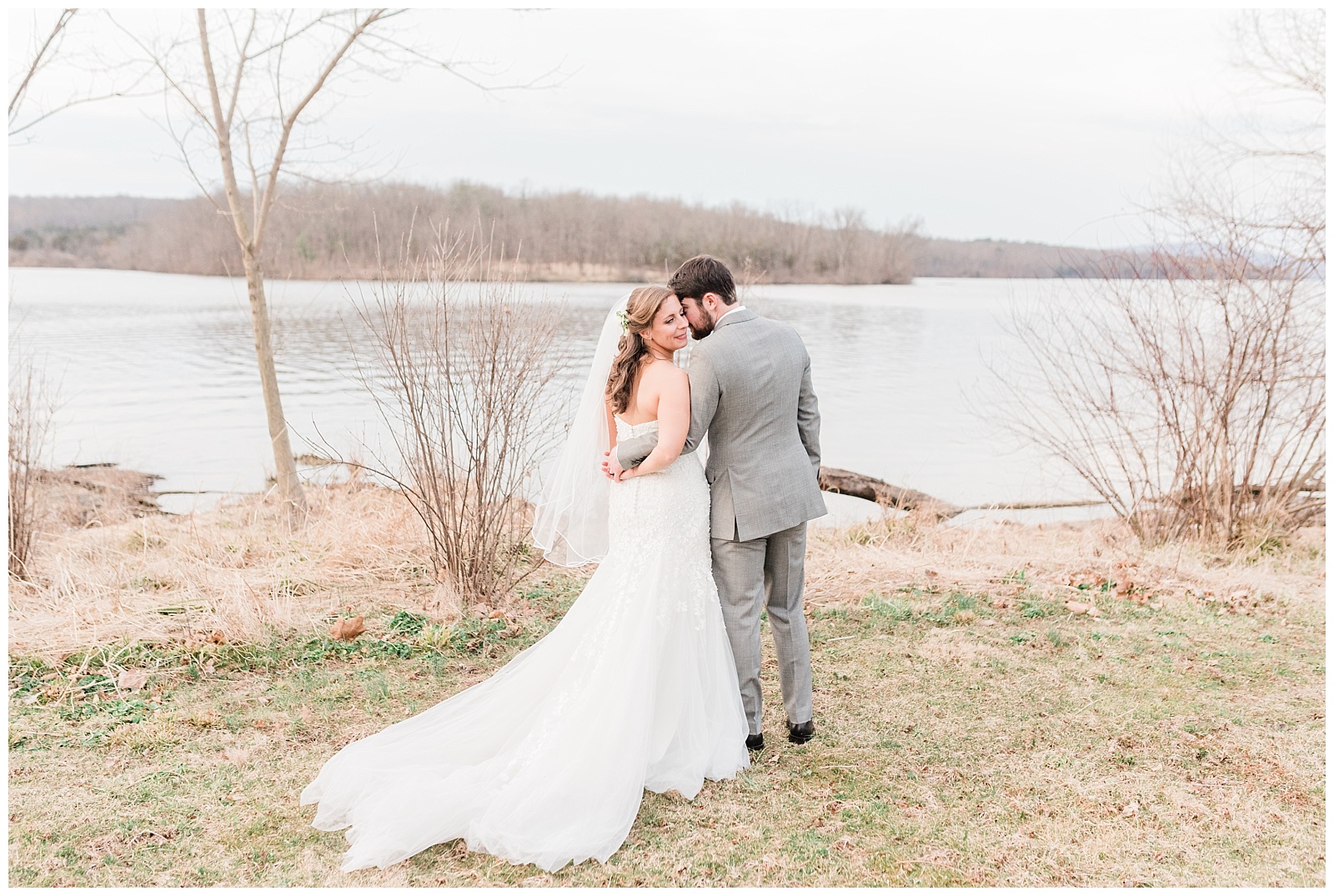 Groom kisses the bride on her cheek in front of the lake at the Lake House Inn wedding venue.