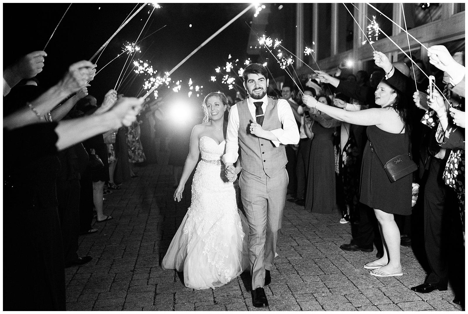 Black and white photo of bride and groom walking through sparkler sendoff at the end of the wedding.