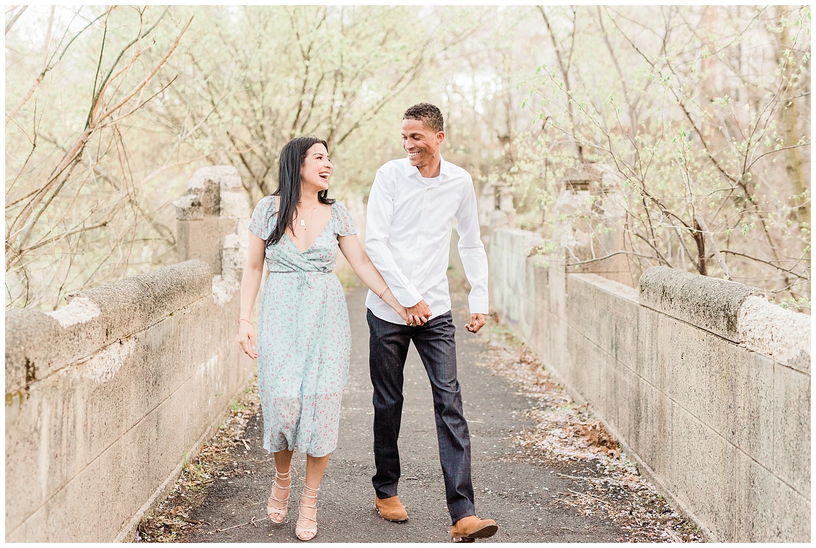 A couple walks across a bridge holding hands and laughing.
