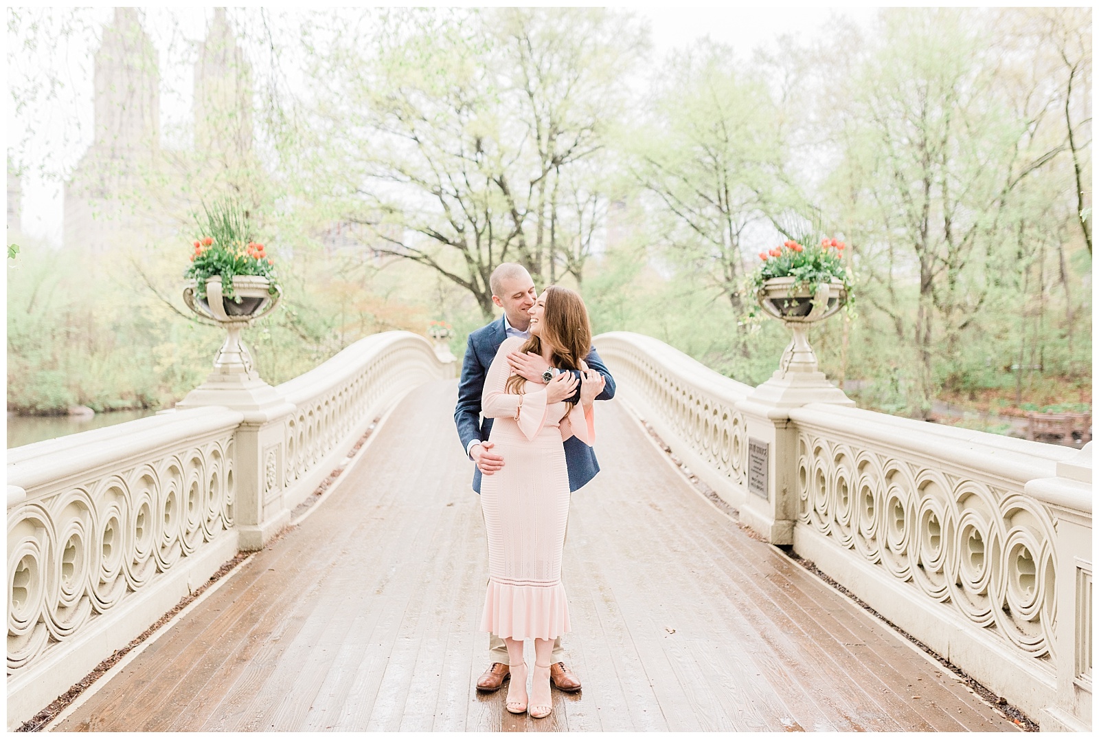 A man hugs his fiancee from behind on Bow Bridge in Central Park.
