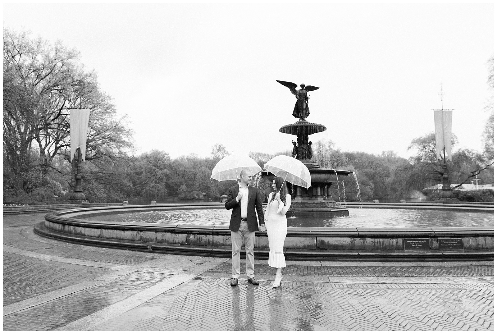 A couple holds hands while under umbrellas in front of Bethesda Fountain.