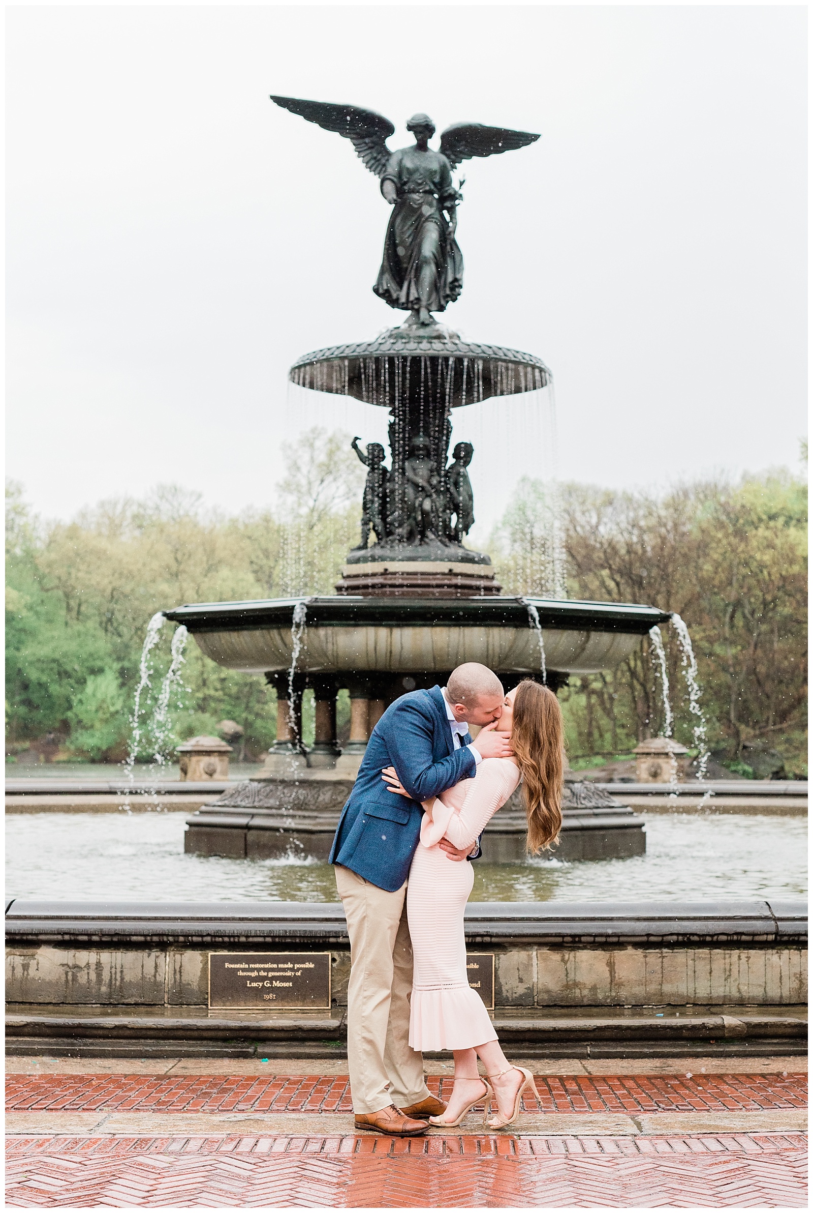 A man dips his fiance back for a kiss in the rain in front of Bethesda Fountain in Central Park, NYC.