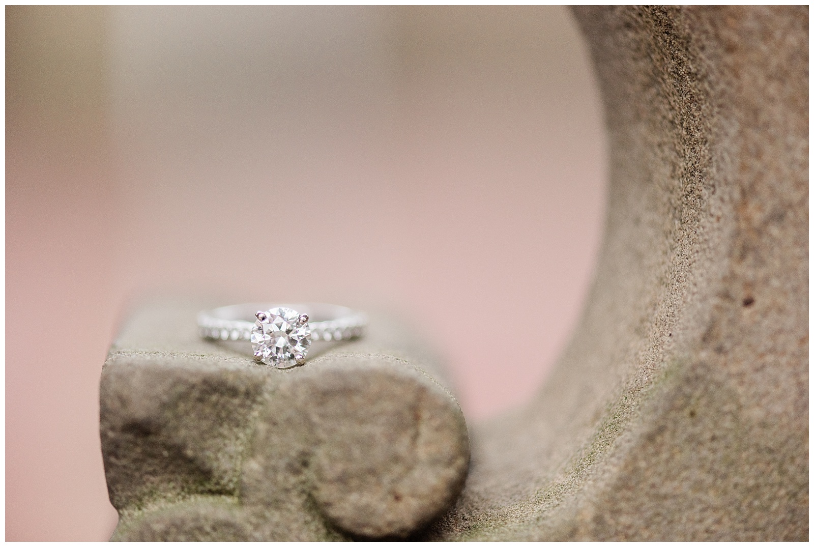 A diamond engagement ring sits on a concrete piece of architecture.