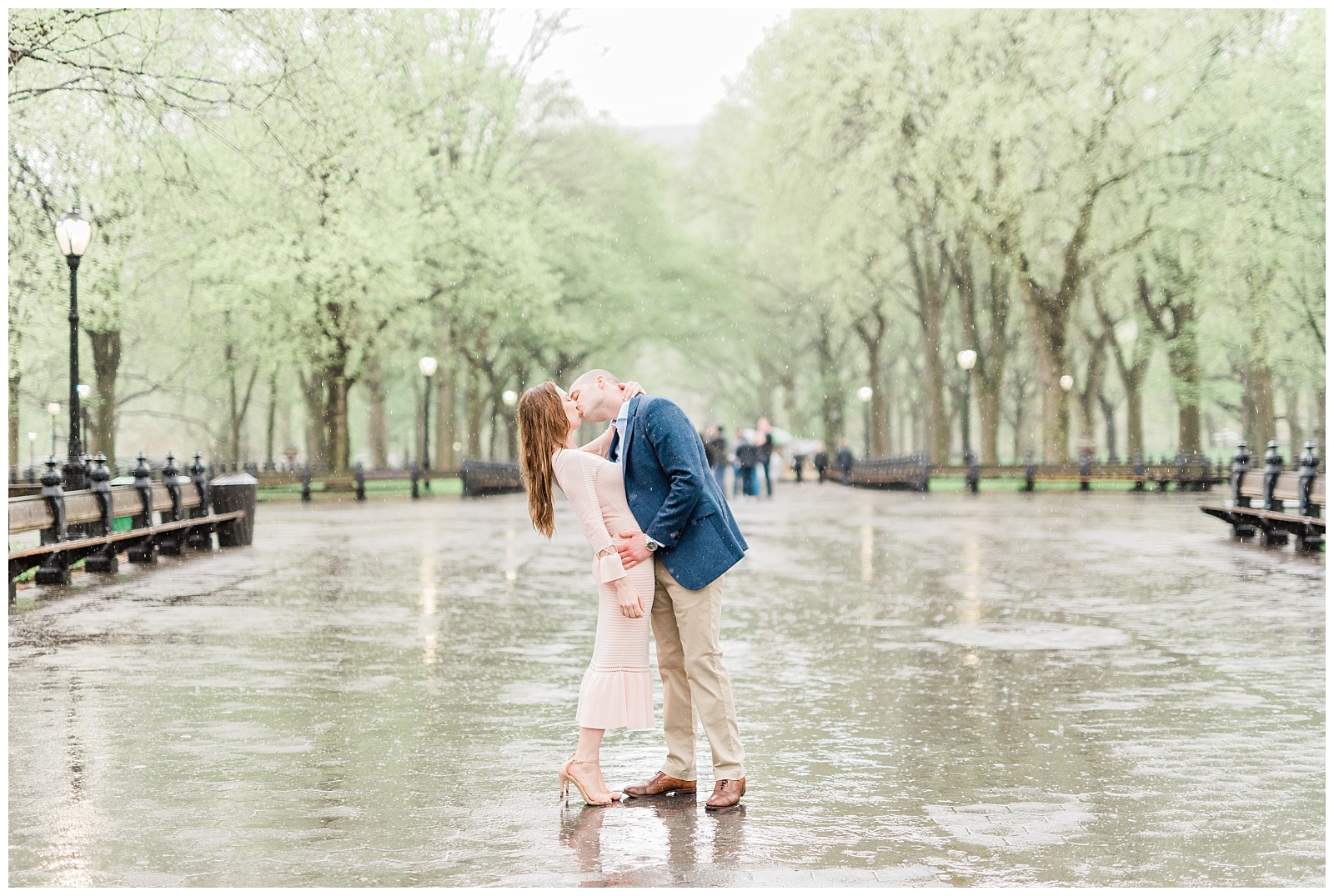 A man dips his fiance back for a romantic kiss in the rain in the Mall at a Central Park.