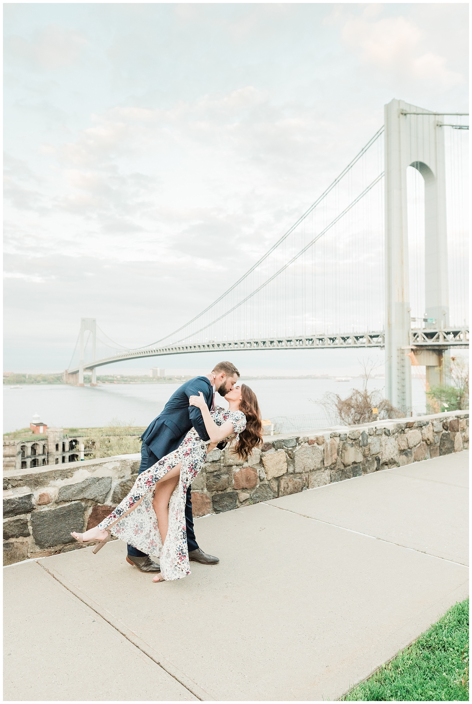 A man dips back his fiancee for a kiss with the Verrazzano Bridge in the background.
