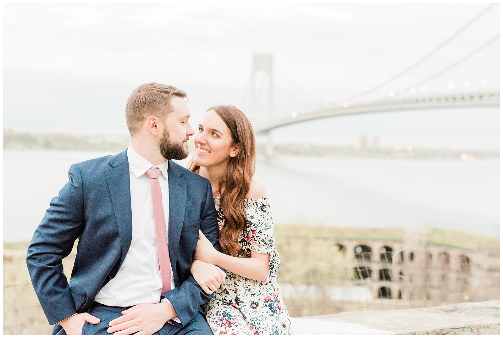 A couple looks at each other while sitting in front of the Verrazzano Bridge.