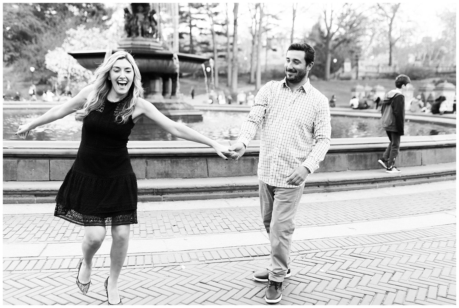 A couple laughs together holding hands in front of Bethesda Fountain in Central Park.