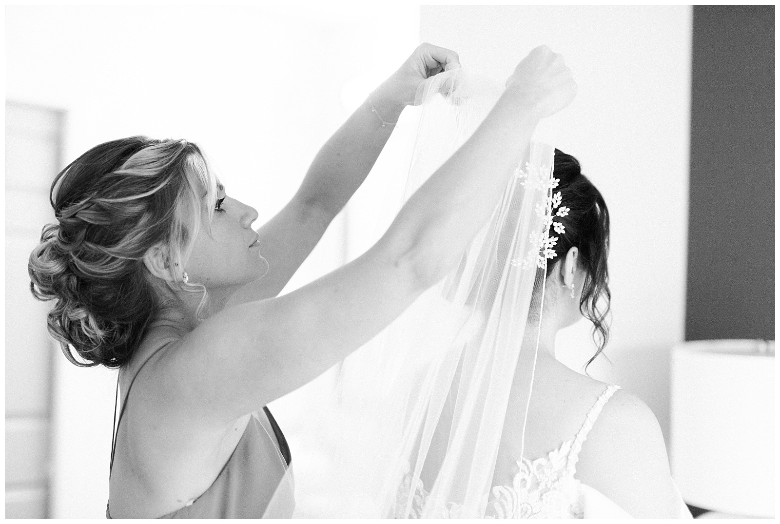 Black and white photo of a bridesmaid putting a veil in the bride's hair.