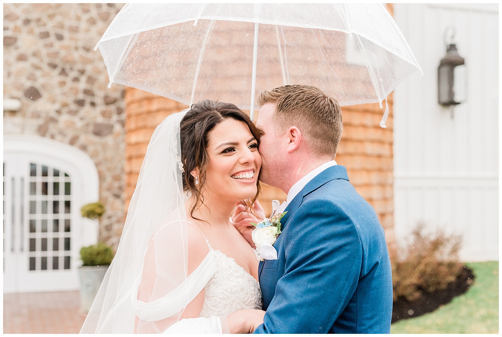 Groom kisses the bride's cheek under a clear umbrella in the rain at the Ryland Inn.