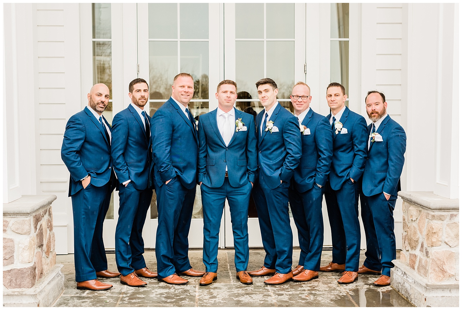 Groomsmen wearing blue suits look at the camera.