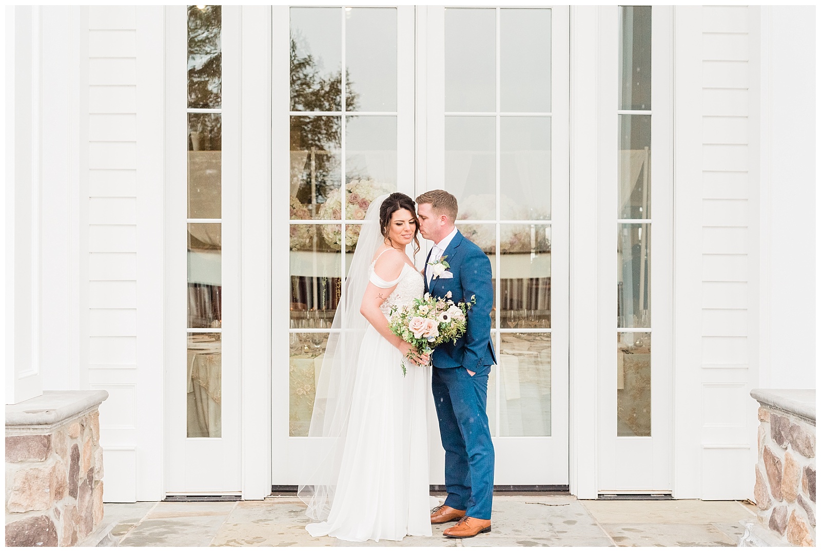 Groom kisses the brides cheek in front of french doors.