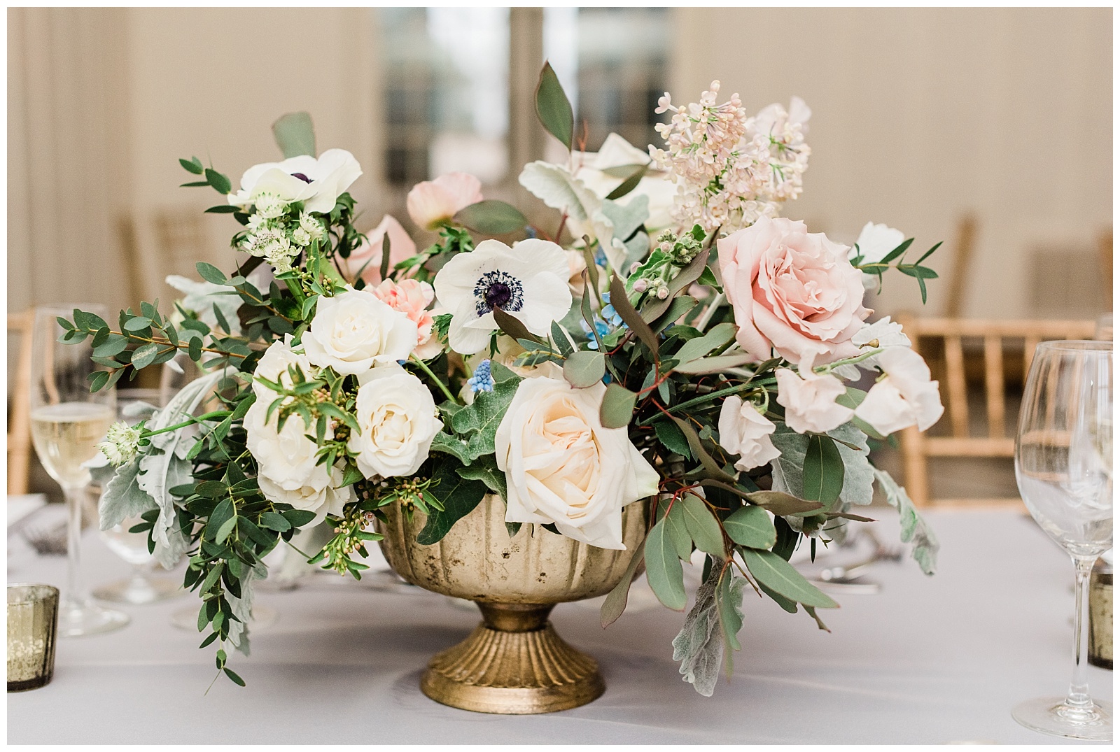 A centerpiece in a gold vase features eucalyptus, anemone flowers, and roses.