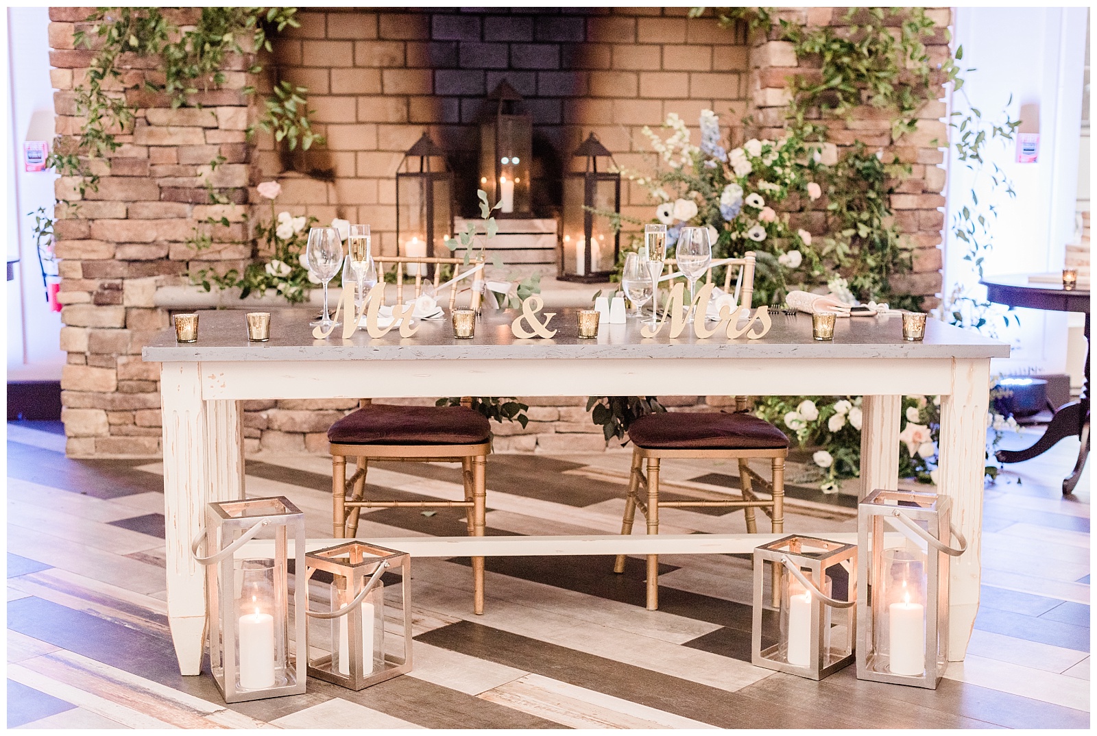 Sweetheart table set up in front of a stone fire place with lanterns and candles.