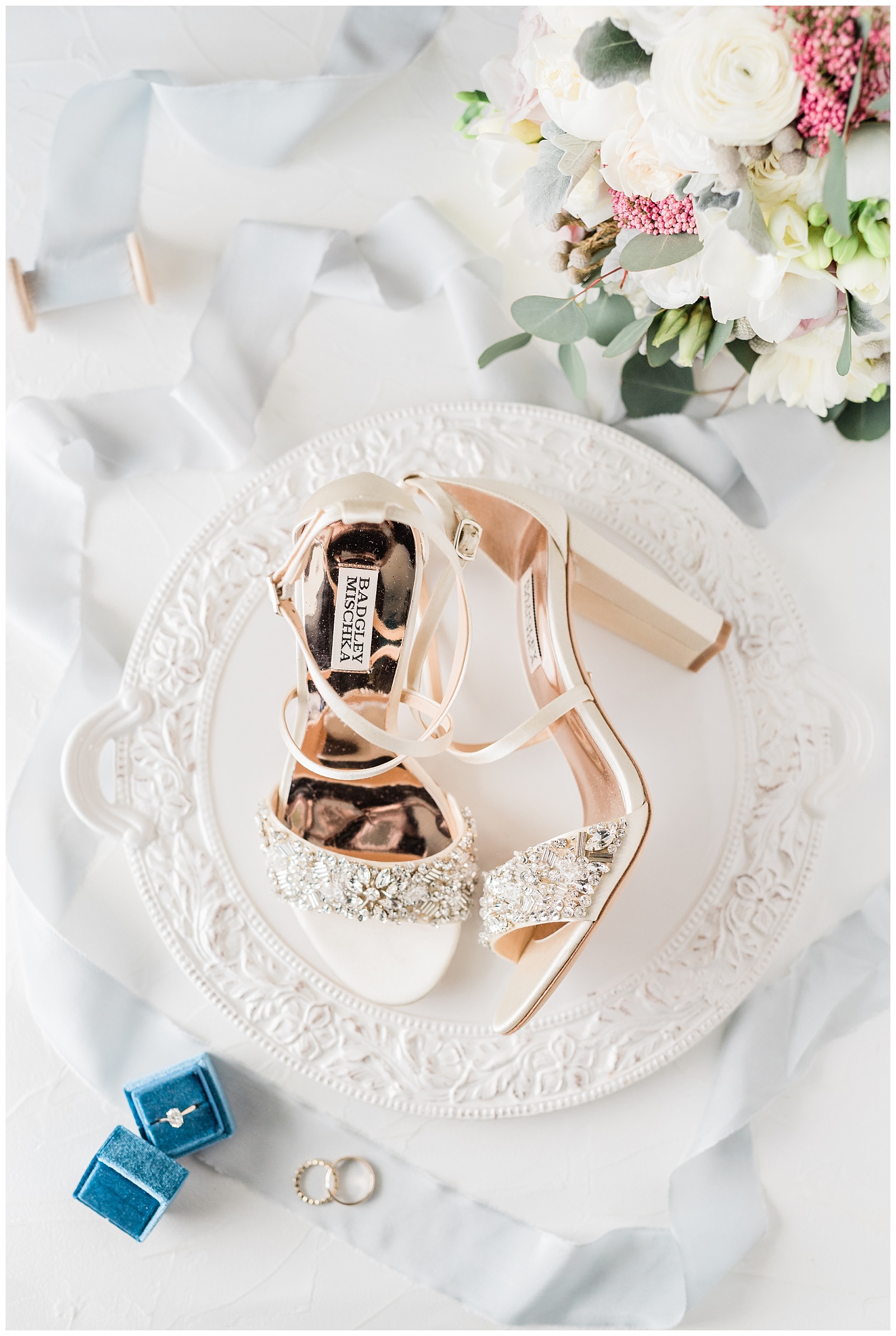 Badgley Mischka high heeled shoes styled on a white tray with flowers and a blue velvet ring box.