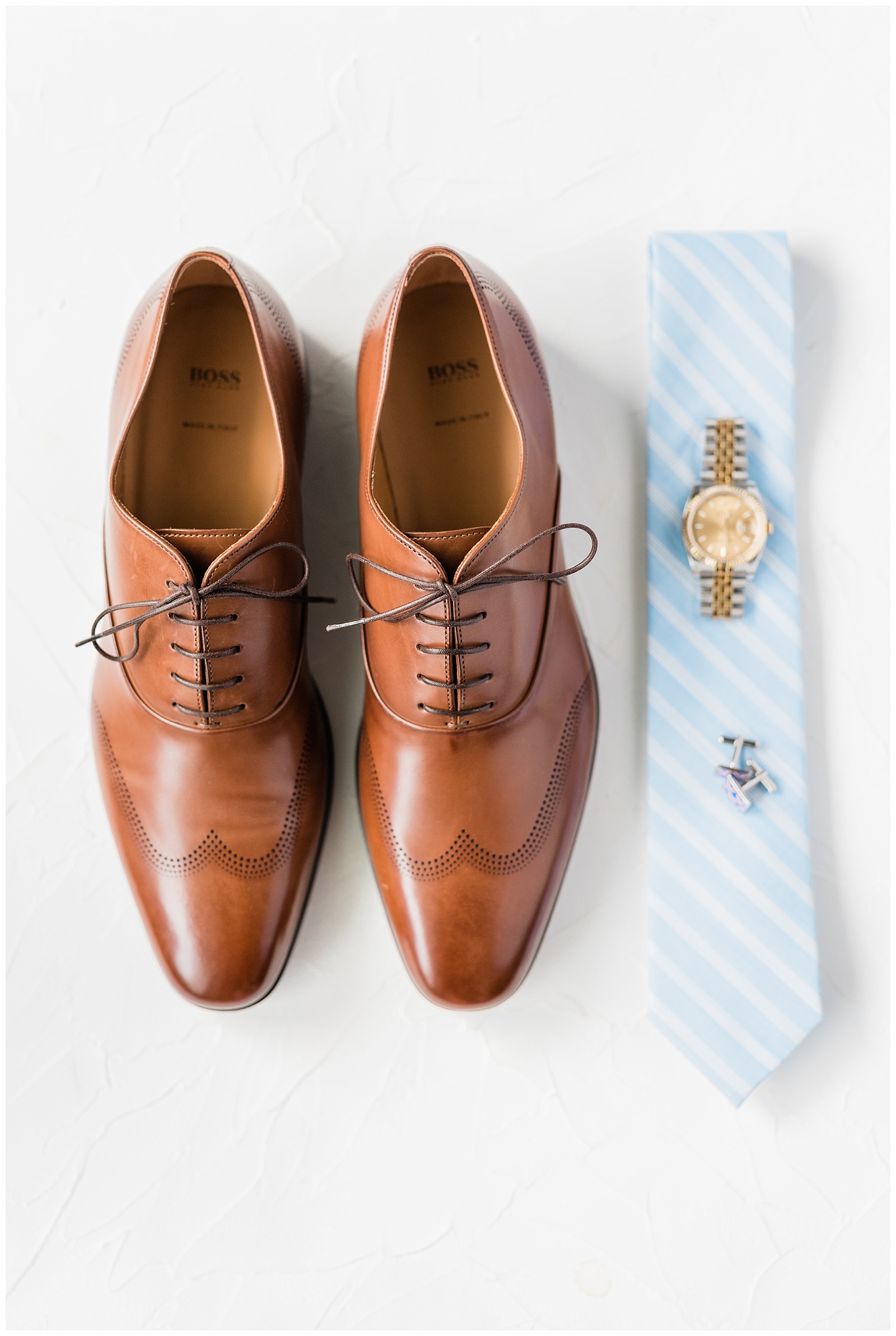 Groom's brown wedding shoes styled with his light blue striped tie, gold watch, and cufflinks.