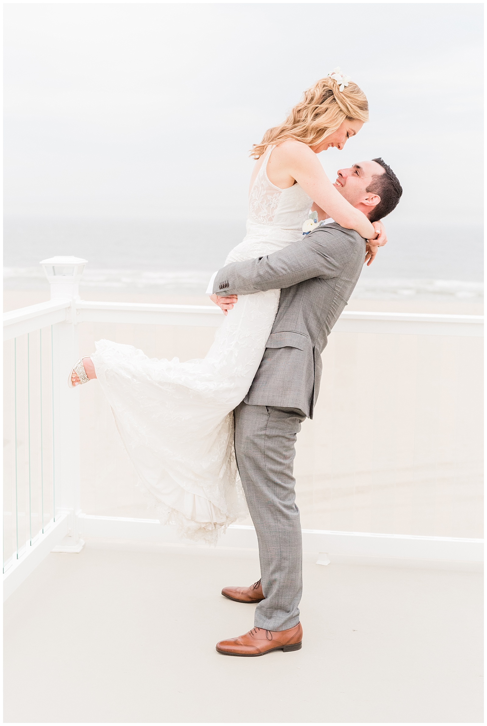Groom lifts up the bride on a deck overlooking the beach.