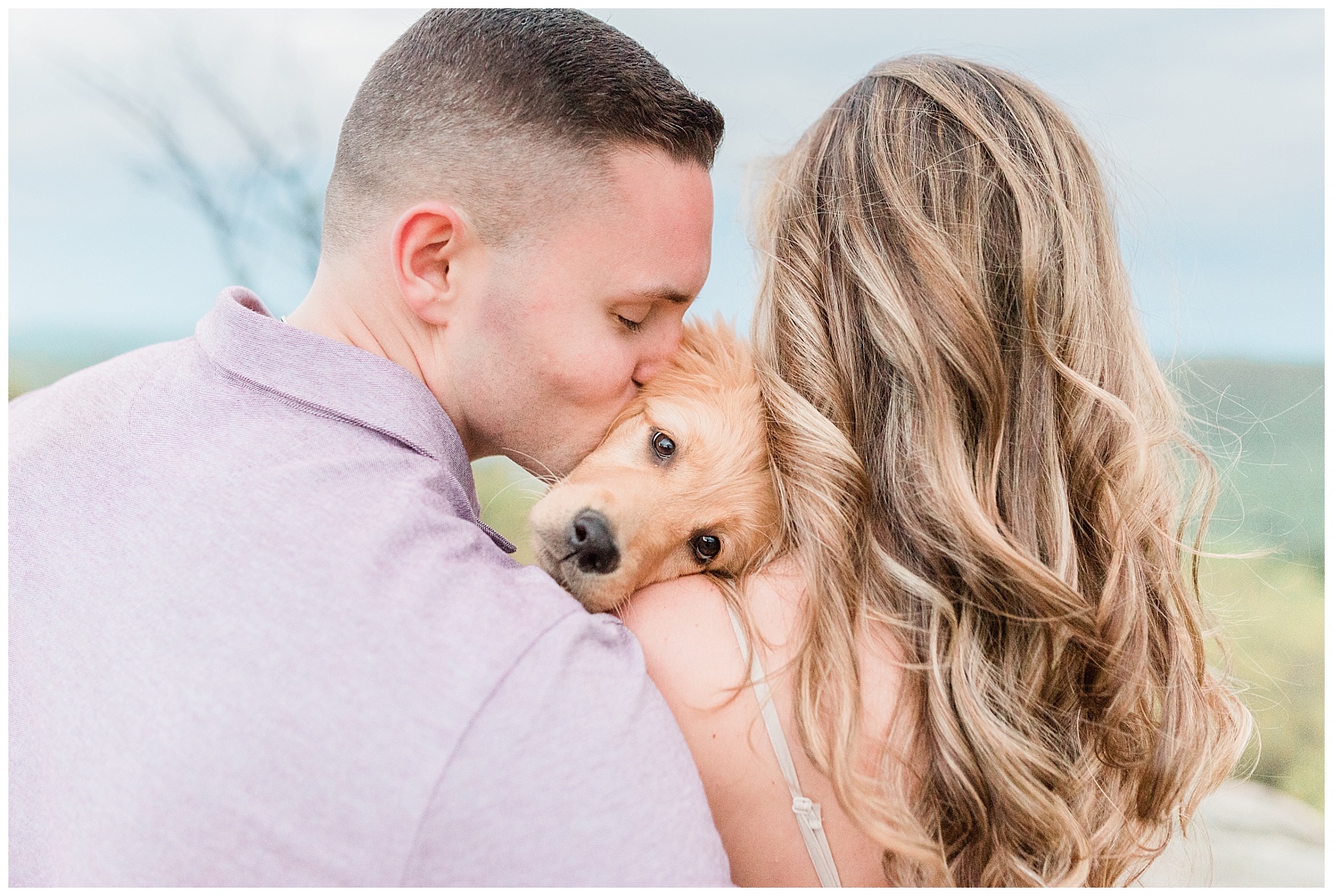 A couple holds a golden retriever puppy and kisses her on the side of the head.