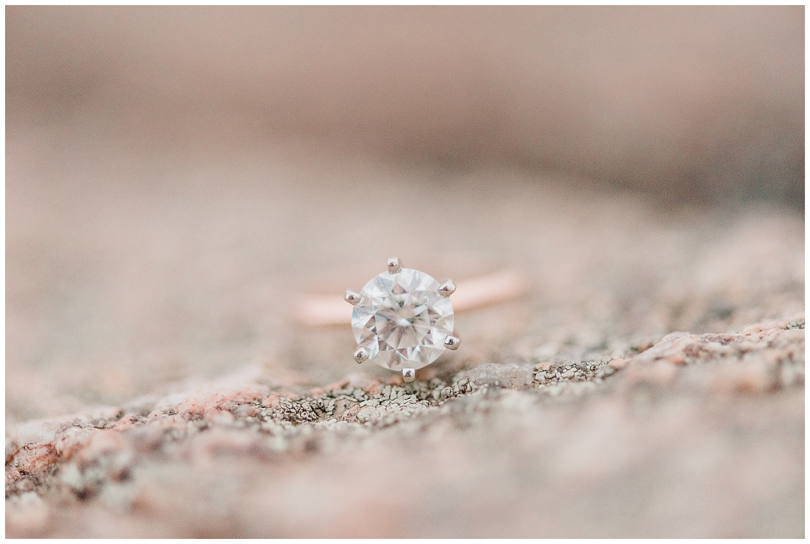 A diamond engagement ring sits on a pink colored rock.