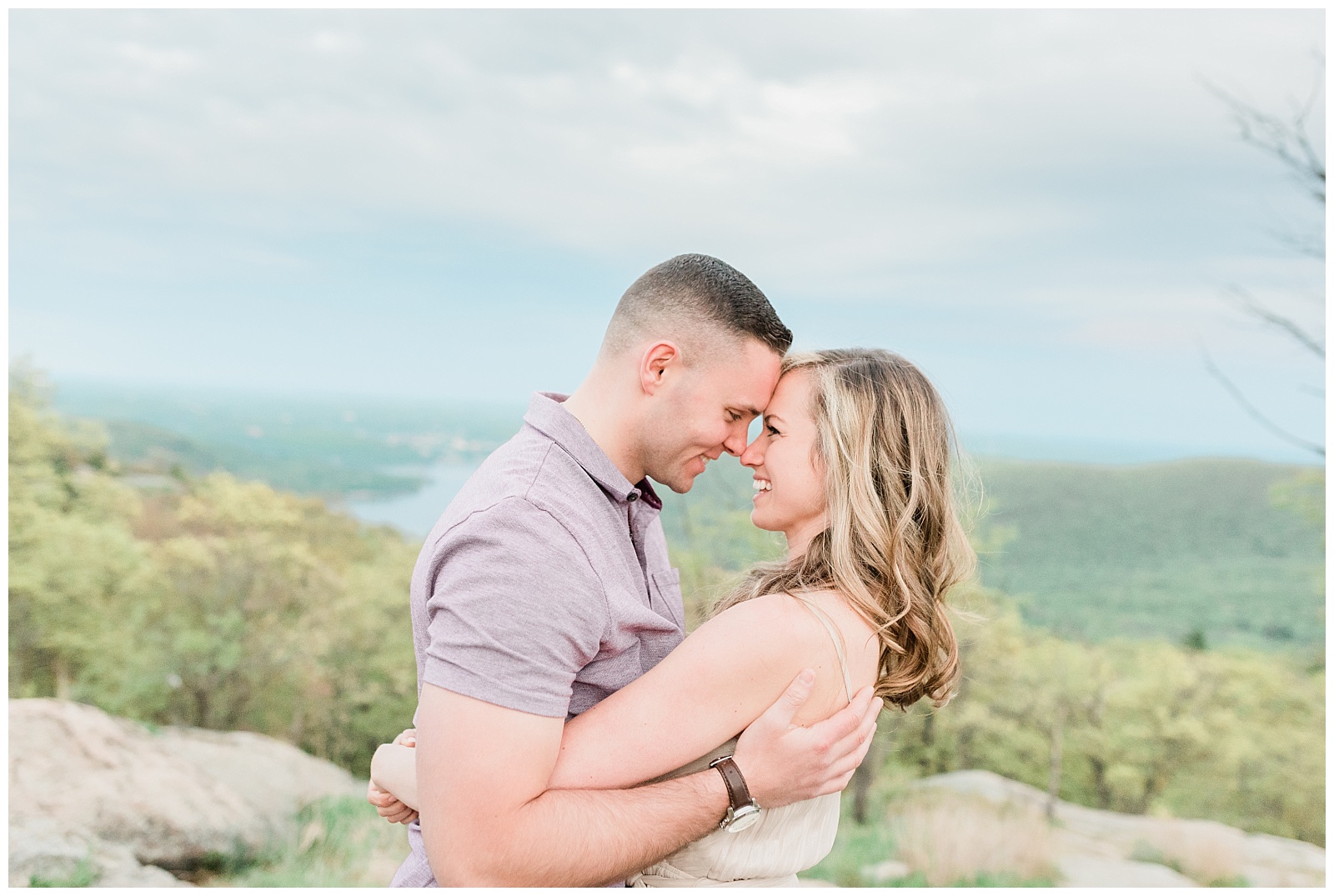 A couple holds each other and rests their foreheads together on a mountaintop.