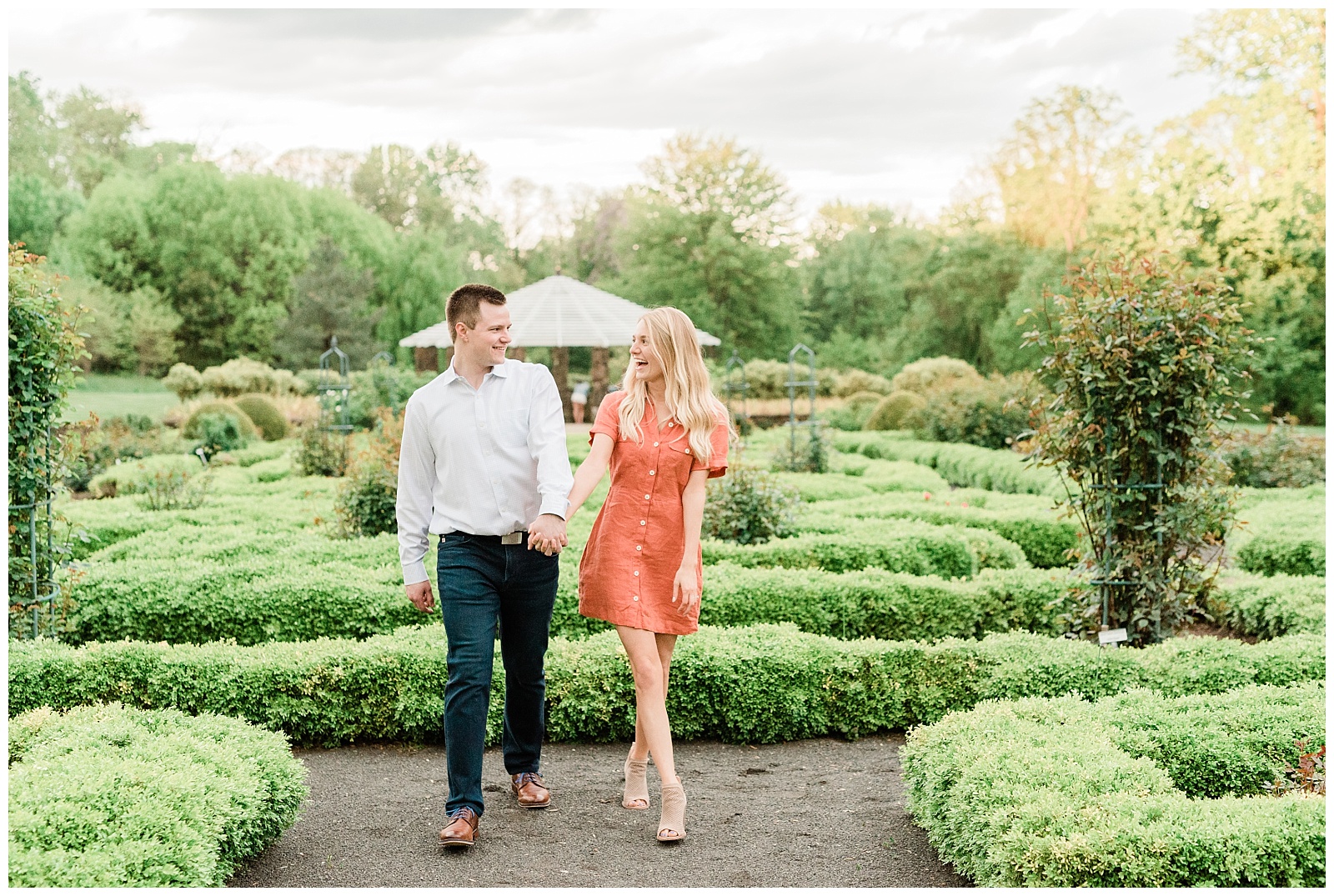 A couple holds hands walking through a garden, laughing together.