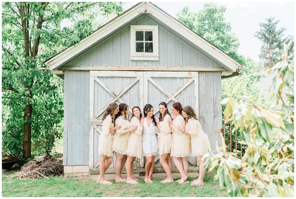 A bride and her bridesmaids pose for a photo in front of a blue shed.
