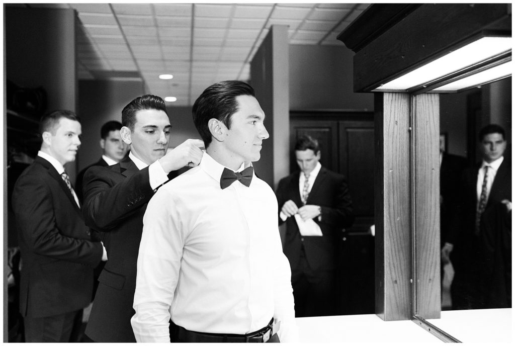 The best man helps the groom with his bow tie.