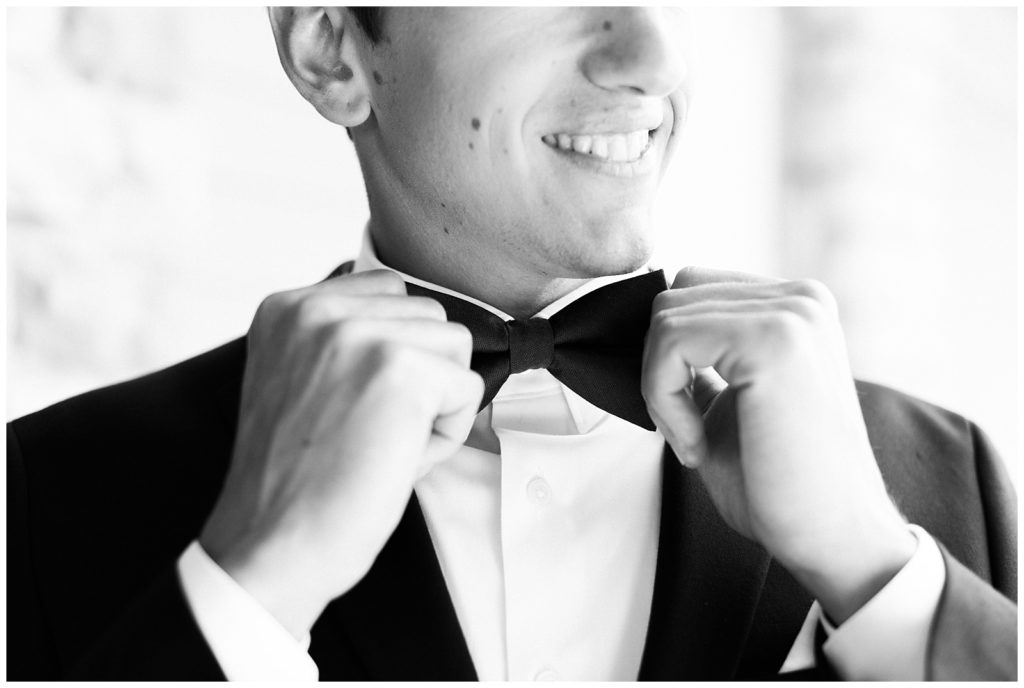 The groom adjusts his bow tie on his wedding day.