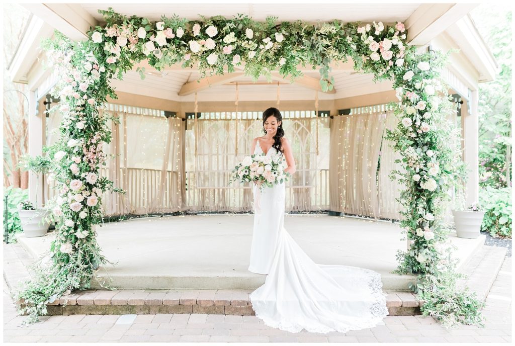A bride stands beneath a floral arch holding her bouquet on her wedding day at Scotland Run.