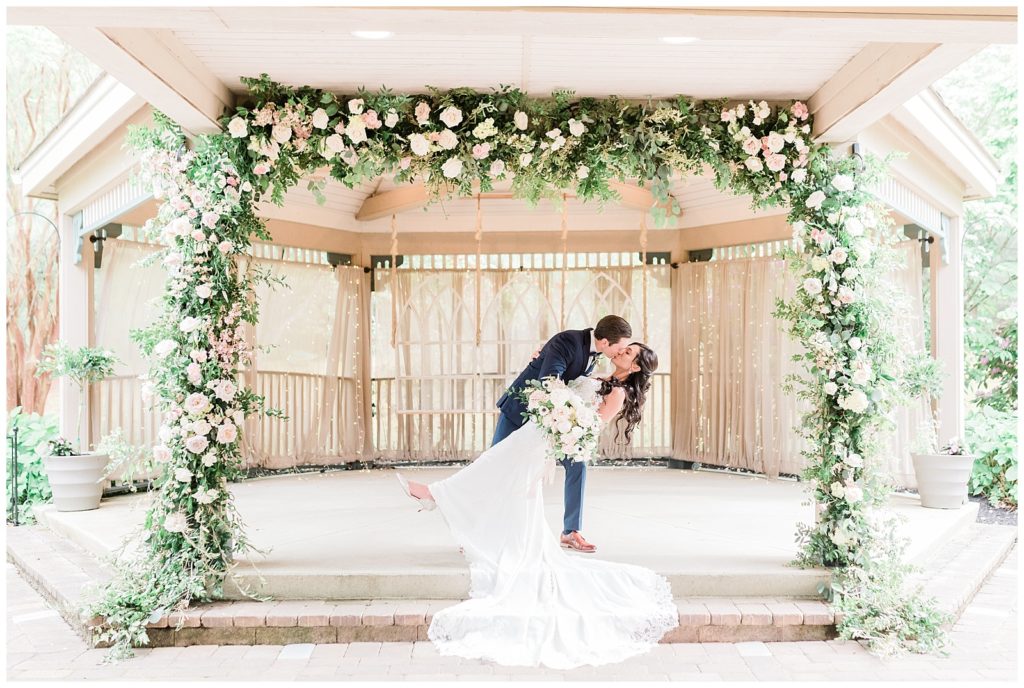 The groom dips the bride back for a kiss beneath the floral ceremony arbor.
