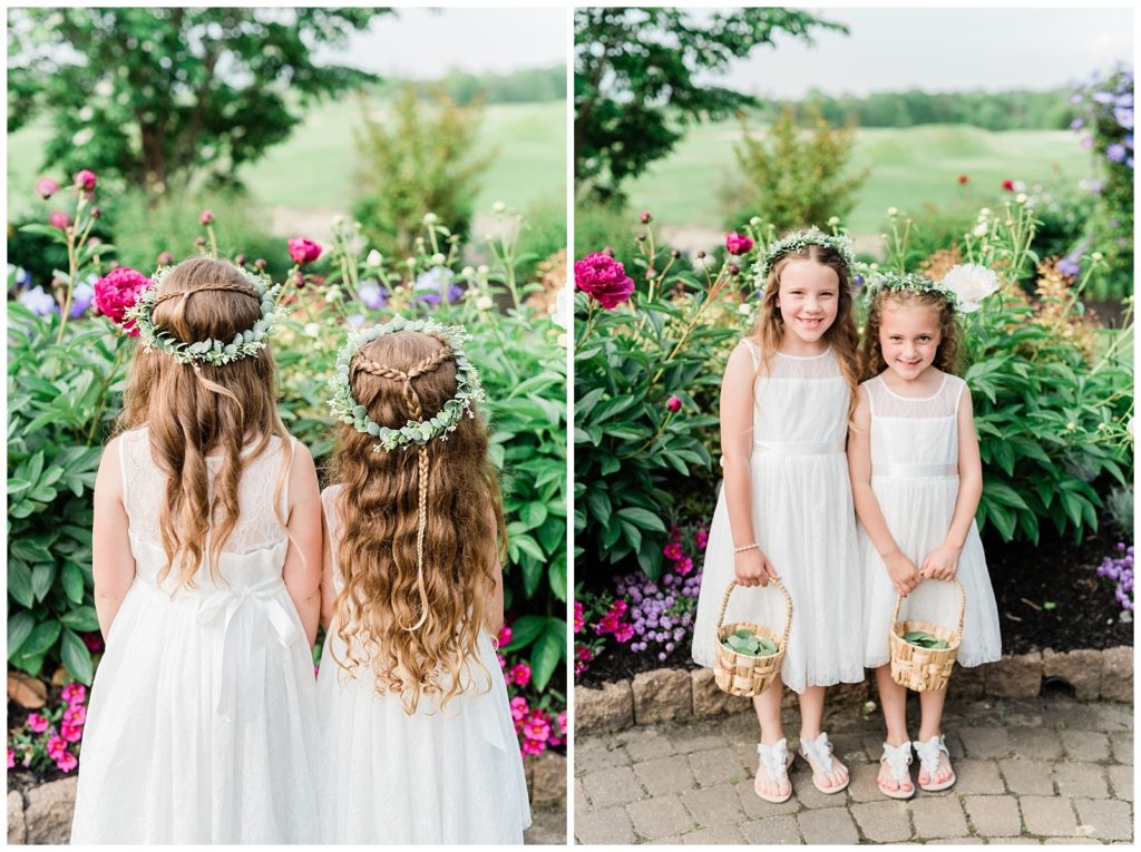 Flower girls wearing flower crowns pose for a photo together in a garden of flowers.