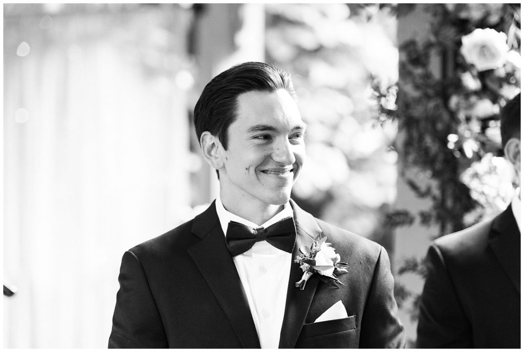 A groom smiles at his bride walking down the aisle during their wedding ceremony.