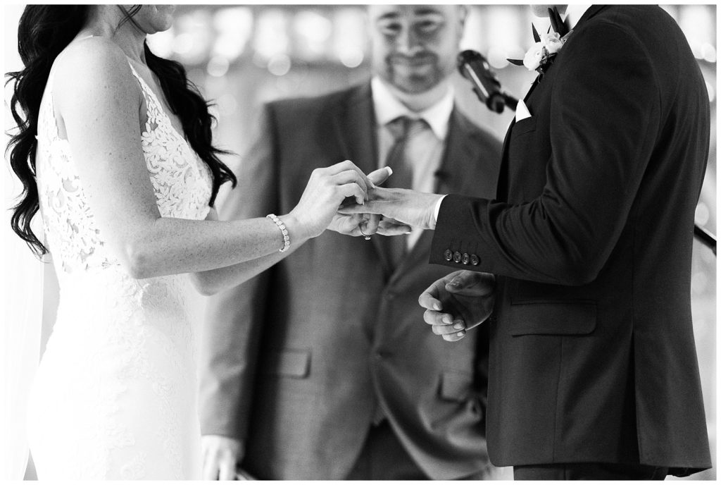 A bride places a wedding band on her groom's finger.
