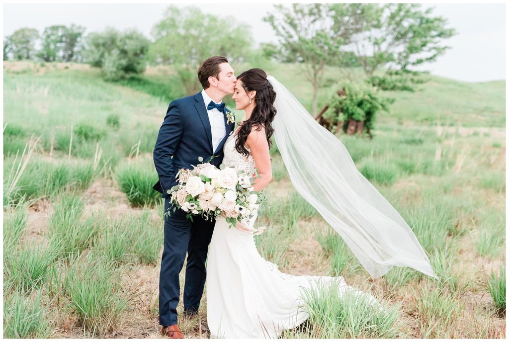 The groom kisses his bride on the forehead in a field of tall grass.
