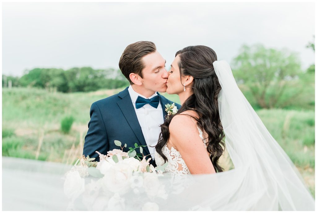 A bride and groom kiss while her veil  is caught in the wind.