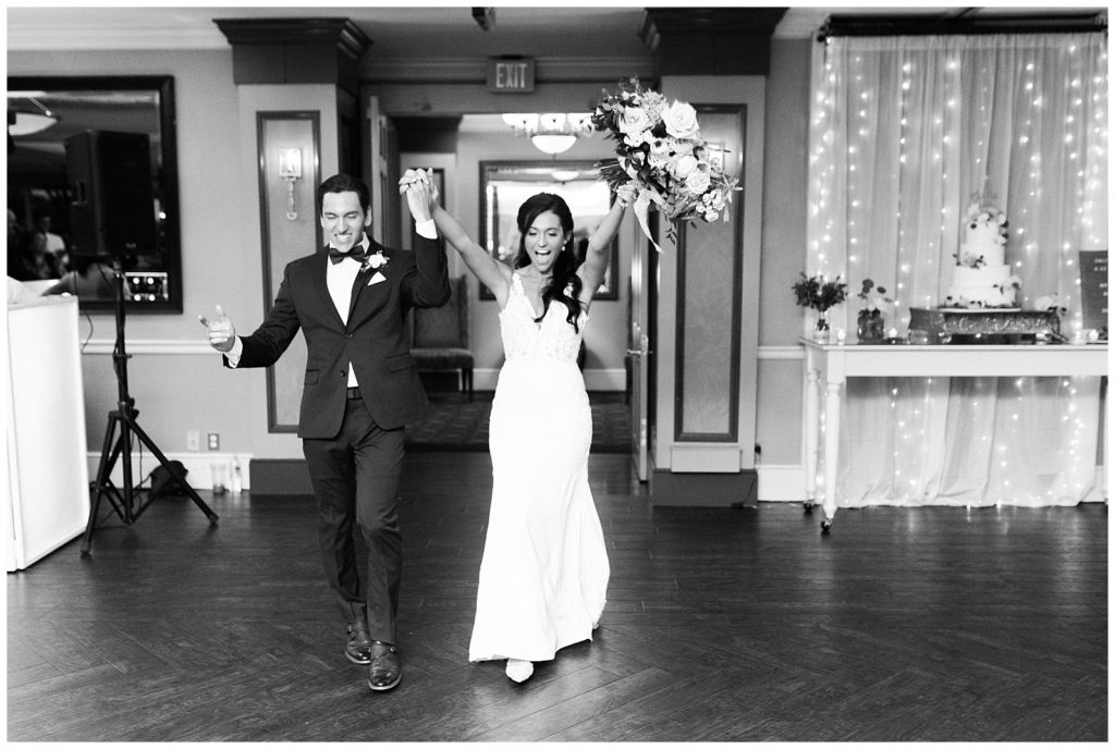 A bride and groom enter their wedding reception cheering and holding their hands up.