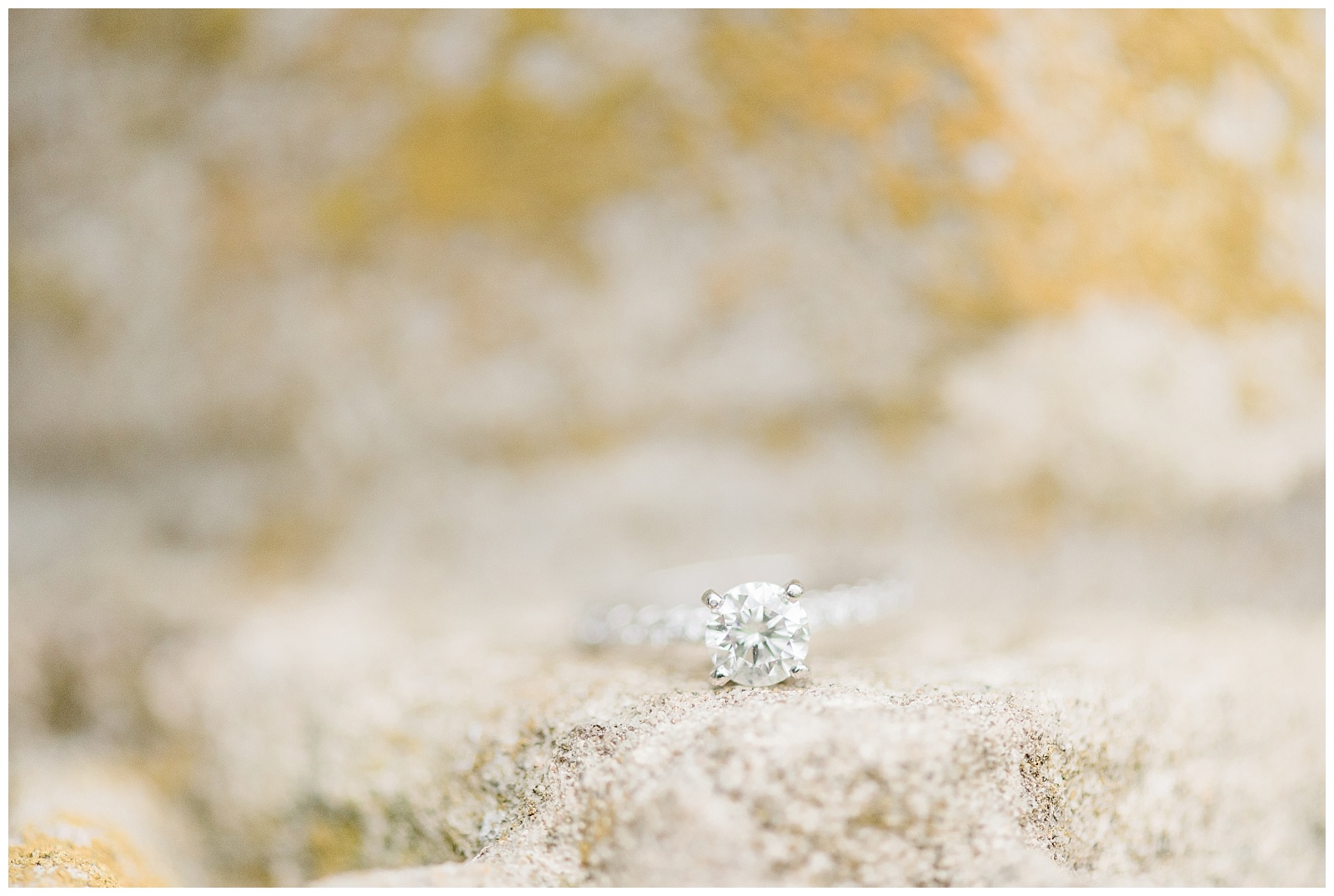 A diamond engagement ring sits on a concrete fountain wall.