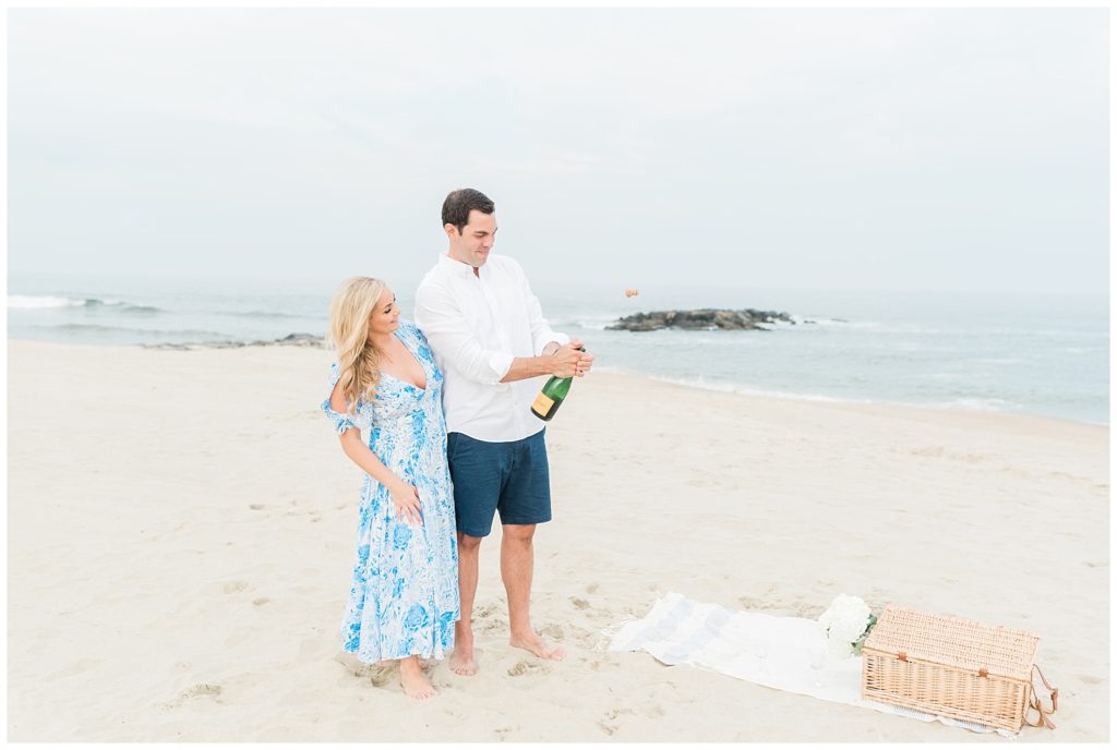 A man pops open a bottle of champagne on the beach.